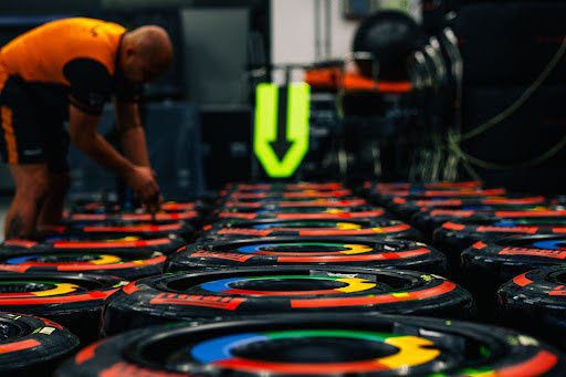 A line of race car wheels with the blue, green, yellow and red Chrome-inspired logo colors around them. A person in an orange shirt is doing maintenance on one of them.